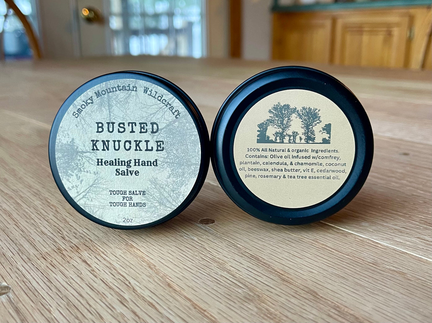 two circle tins of a product call "busted Knuckle healing hand salve" made by Smoky Mountain WIldcraft. Photo is of the front and back of the tin.