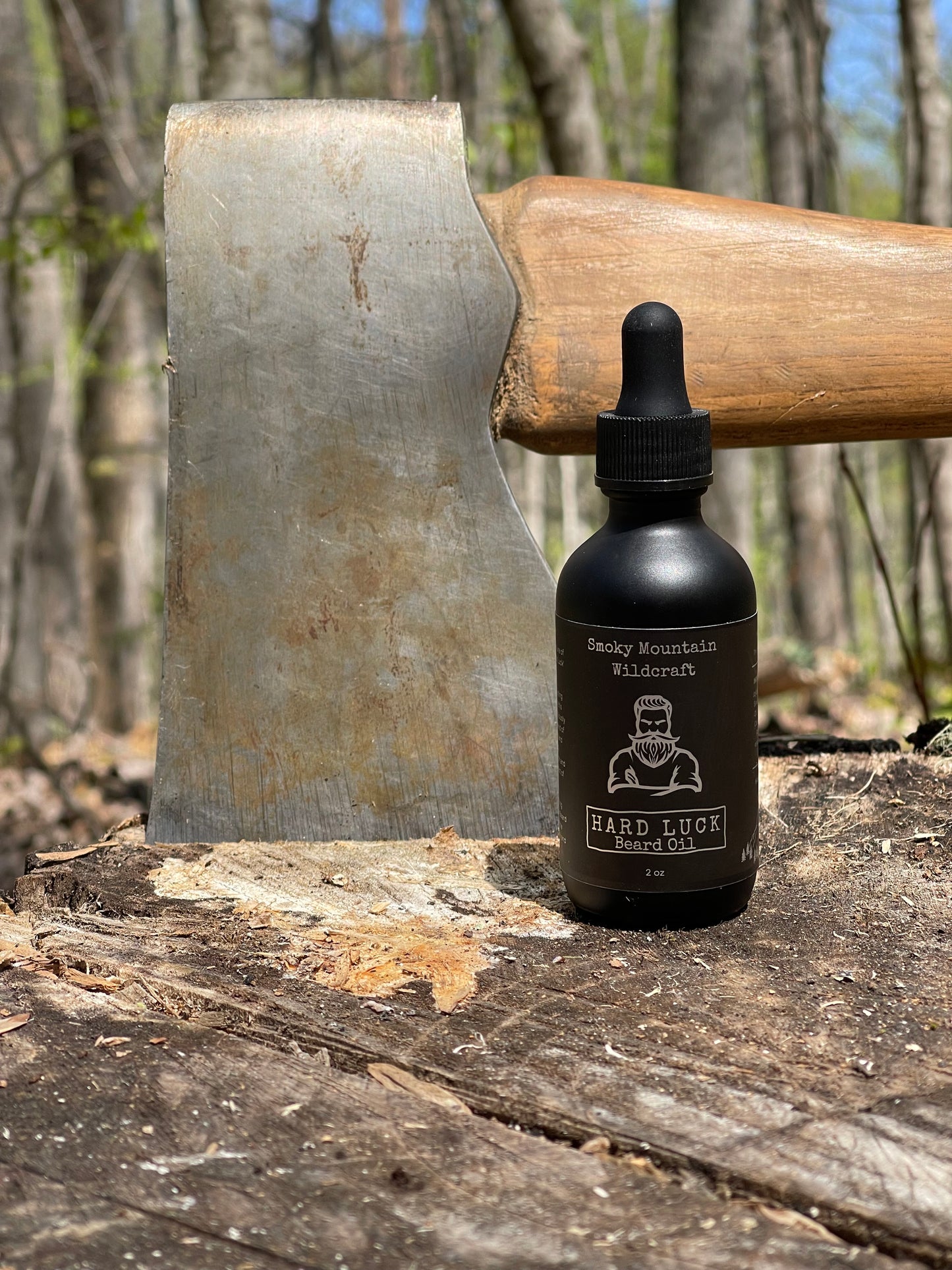 Bottle of Beard Oil product on an stump with an axe in it with a forest background