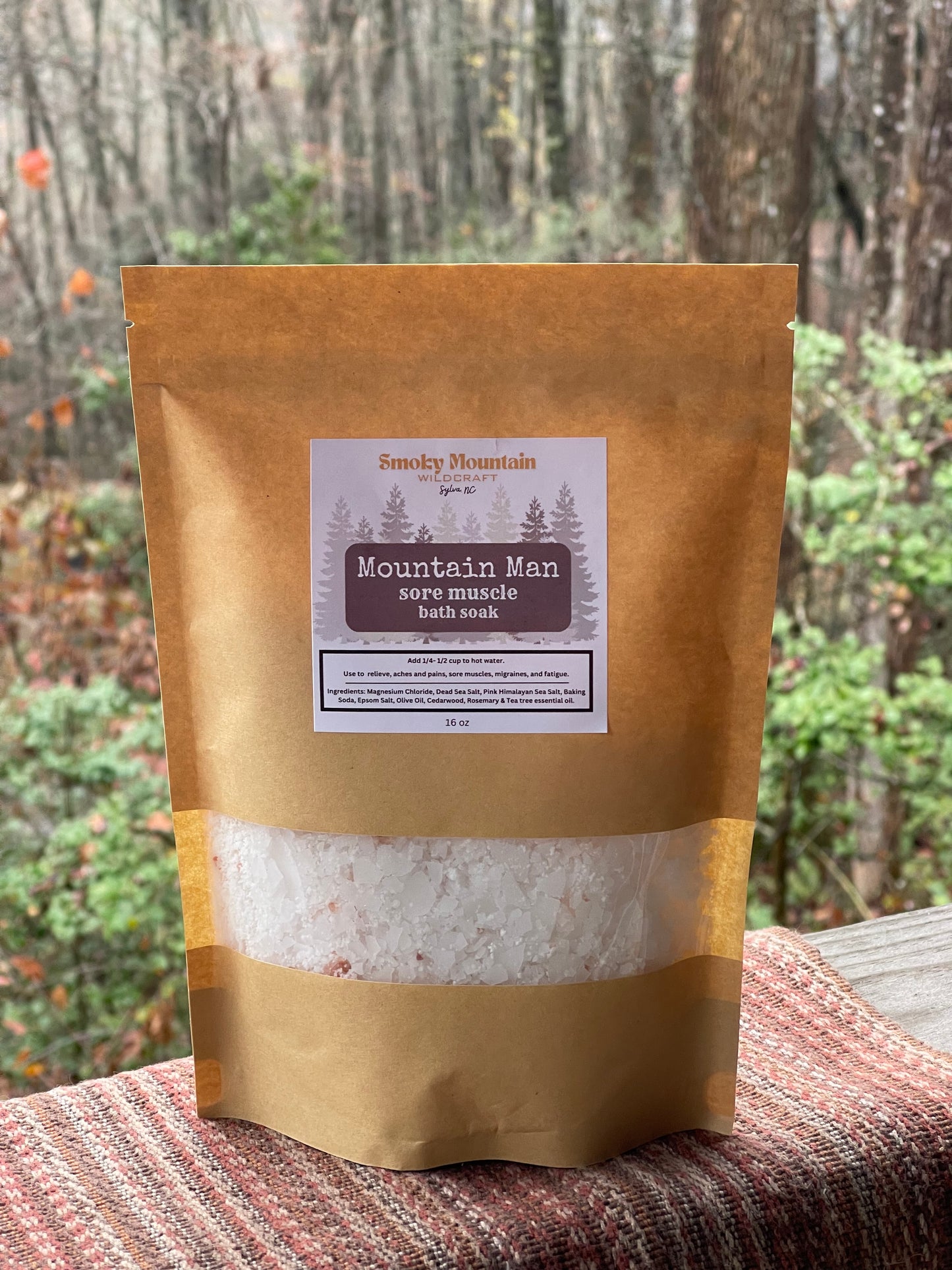 Front view of brown paper pouche of Magnesium Bath Soak, with a clear window showing the product inside. They are placed on a wooden surface with a natural background.
