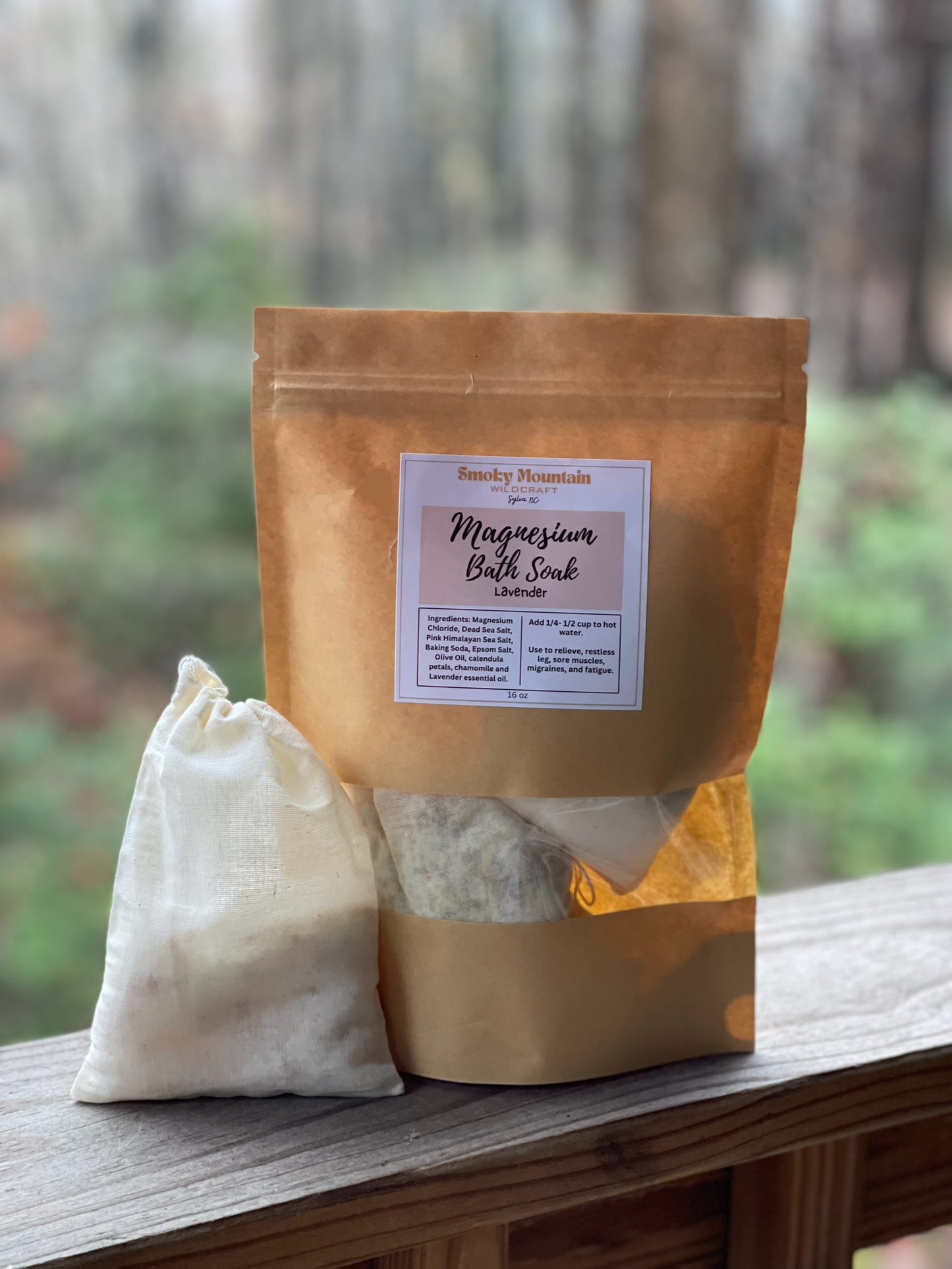 front view of the large bath salt soak in a brown paper bag with a window to view the bath soak. Set in front of a wooded background.