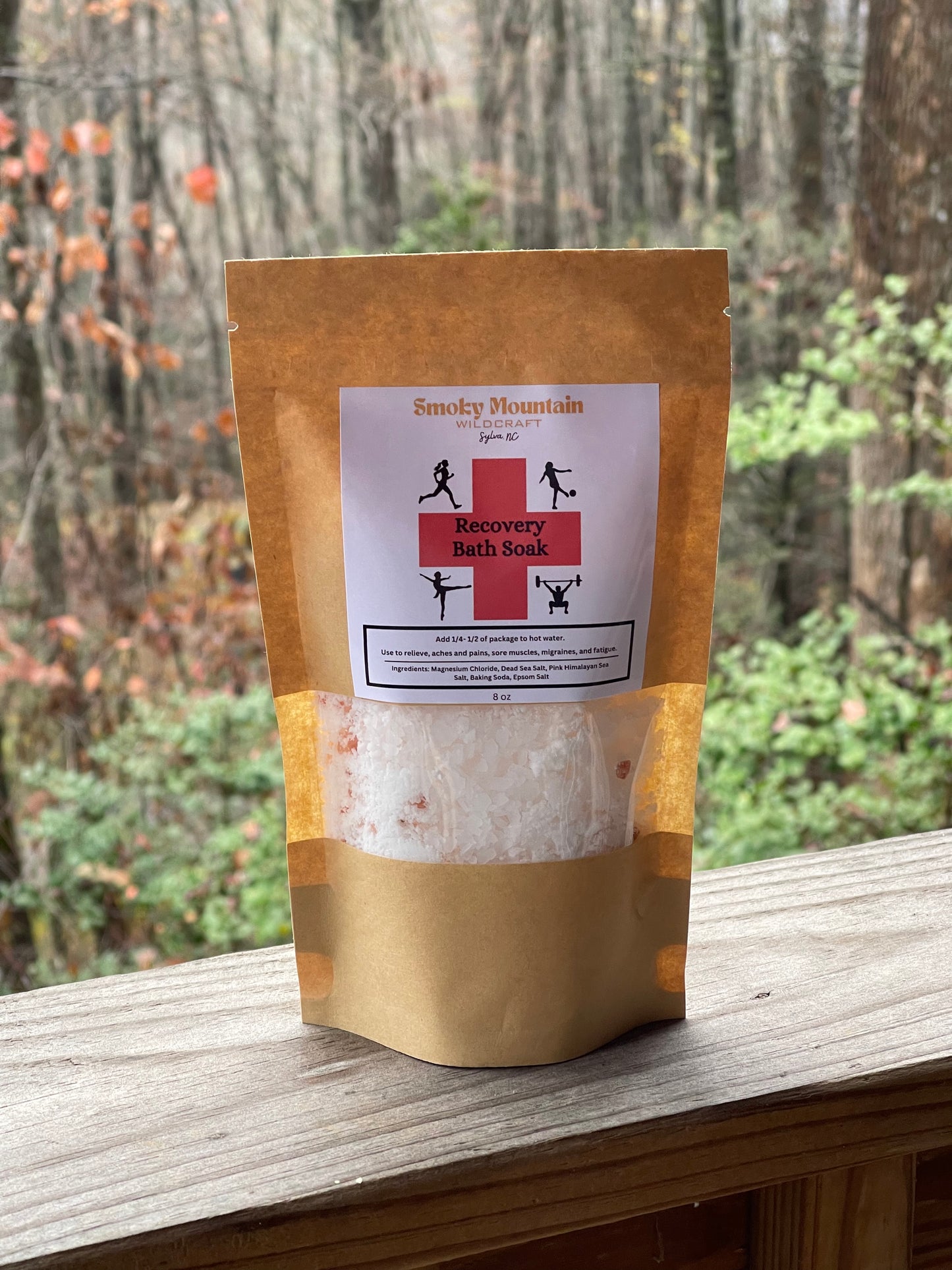 front view of the small size bath salt soak in a brown paper bag with a window to view the bath soak. Set in front of a wooded background.
