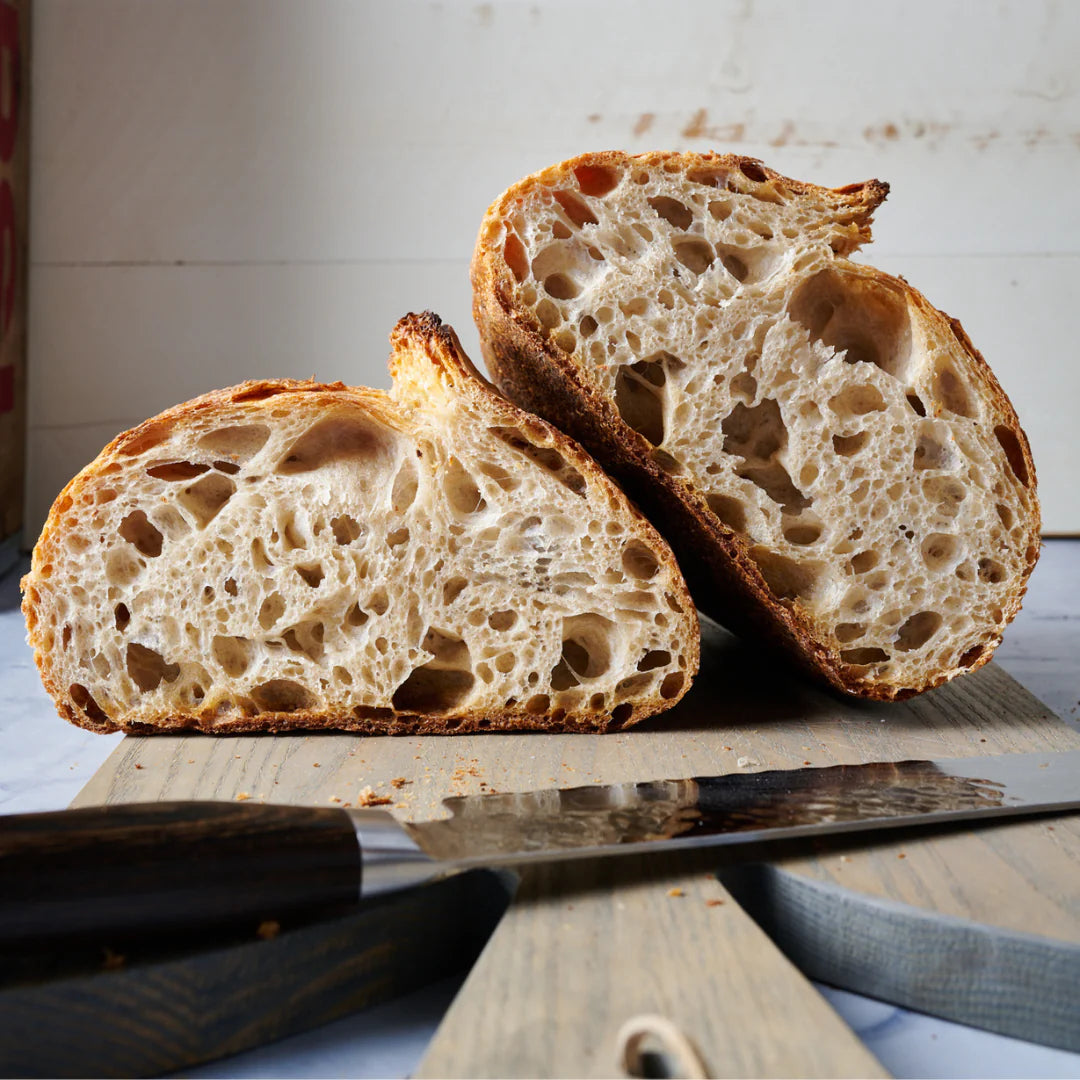 Front view of a cut in half sourdough loaf with one half flat on the table and the other half rested on one side of the other half.