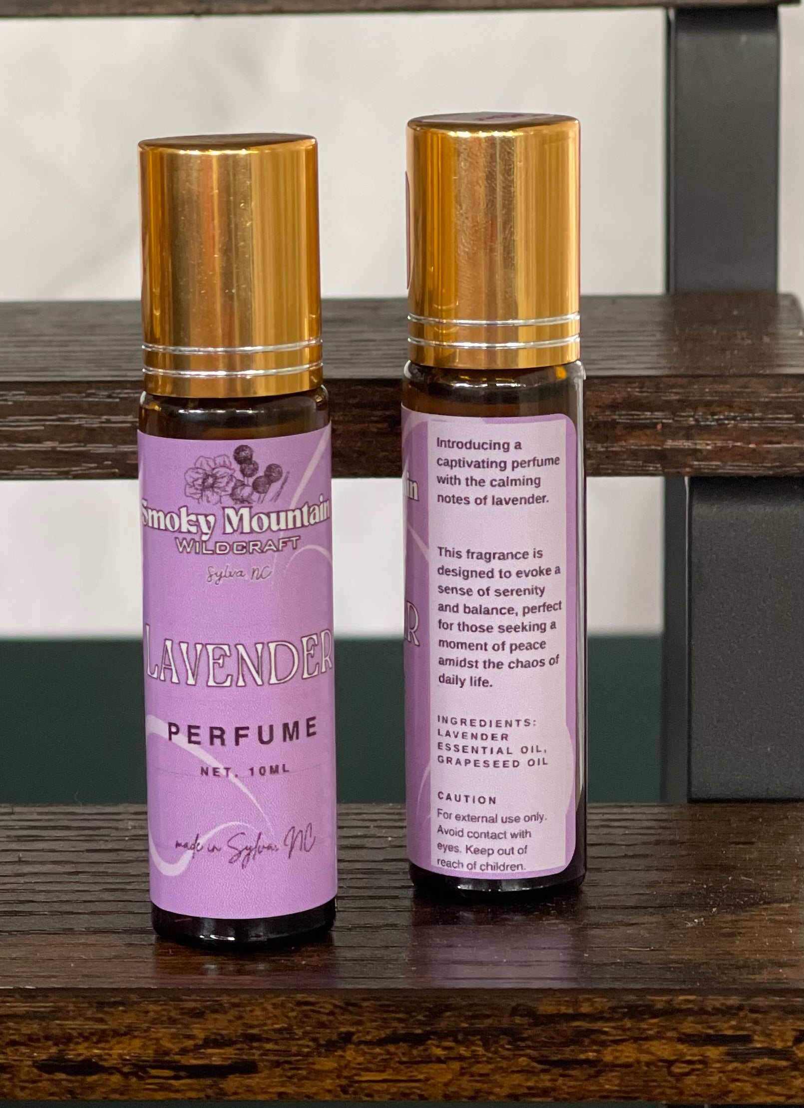 Lavender perfume / fragrance Two amber bottles with gold lids, one bottle is the front of the label and the second is the back of the label.  Roller bottles of an essential oil fragrance / perfume. 