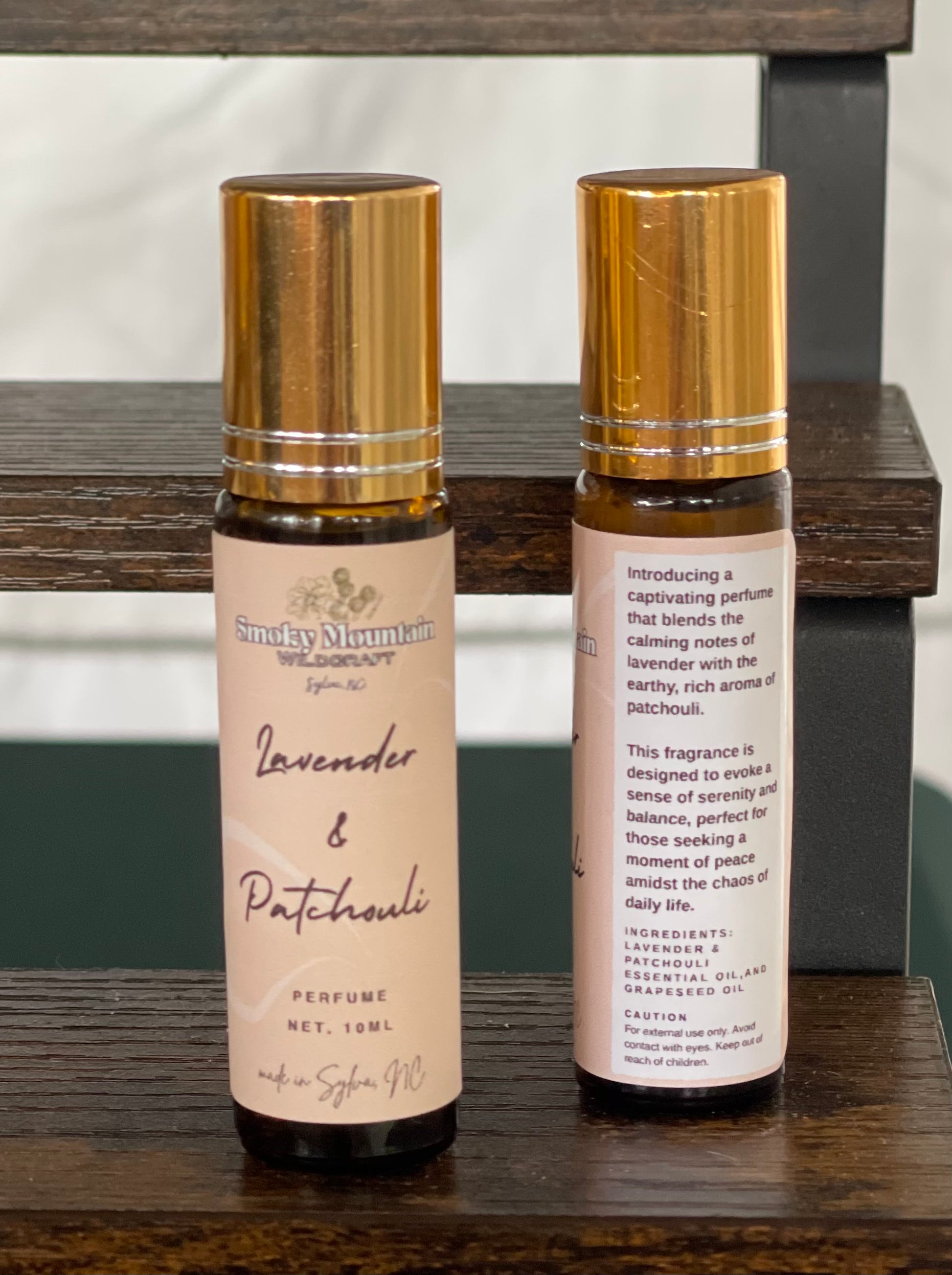 Lavender & Patchouli perfume / fragrance. Photo of two amber bottles with gold lids, one bottle is the front of the label and the second is the back of the label.  Roller bottles of an essential oil fragrance / perfume. 