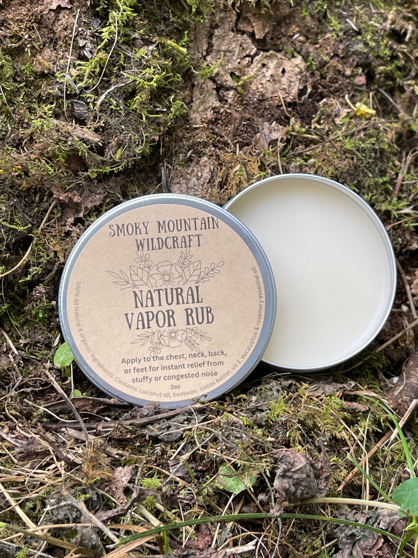 A can of Smokey Mountain Wildcraft Natural Vapor Rub placed on a ground cover with moss, indicating it is a natural product with eucalyptus and rosemary essential oils.