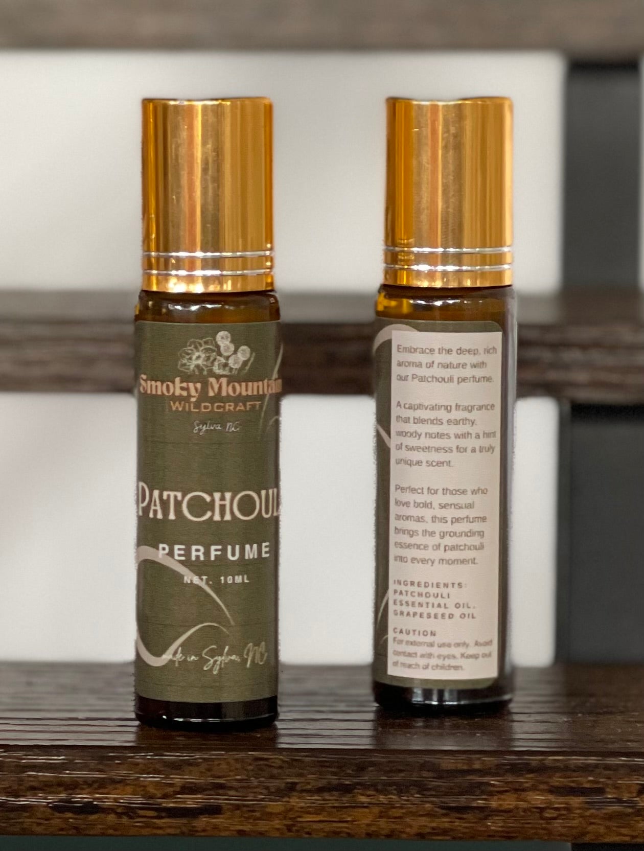 Patchouli perfume / fragrance. Photo of two amber bottles with gold lids, one bottle is the front of the label and the second is the back of the label.  Roller bottles of an essential oil fragrance / perfume. 
