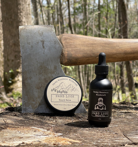Beard care products including a bottle and circle tin on a log with an axe in the background.