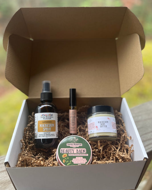 A gift box opened to reveal various items including ,a magnesium spray, lash envy, magnesium body butter, and beauty balm. All placed on natural straw bedding.