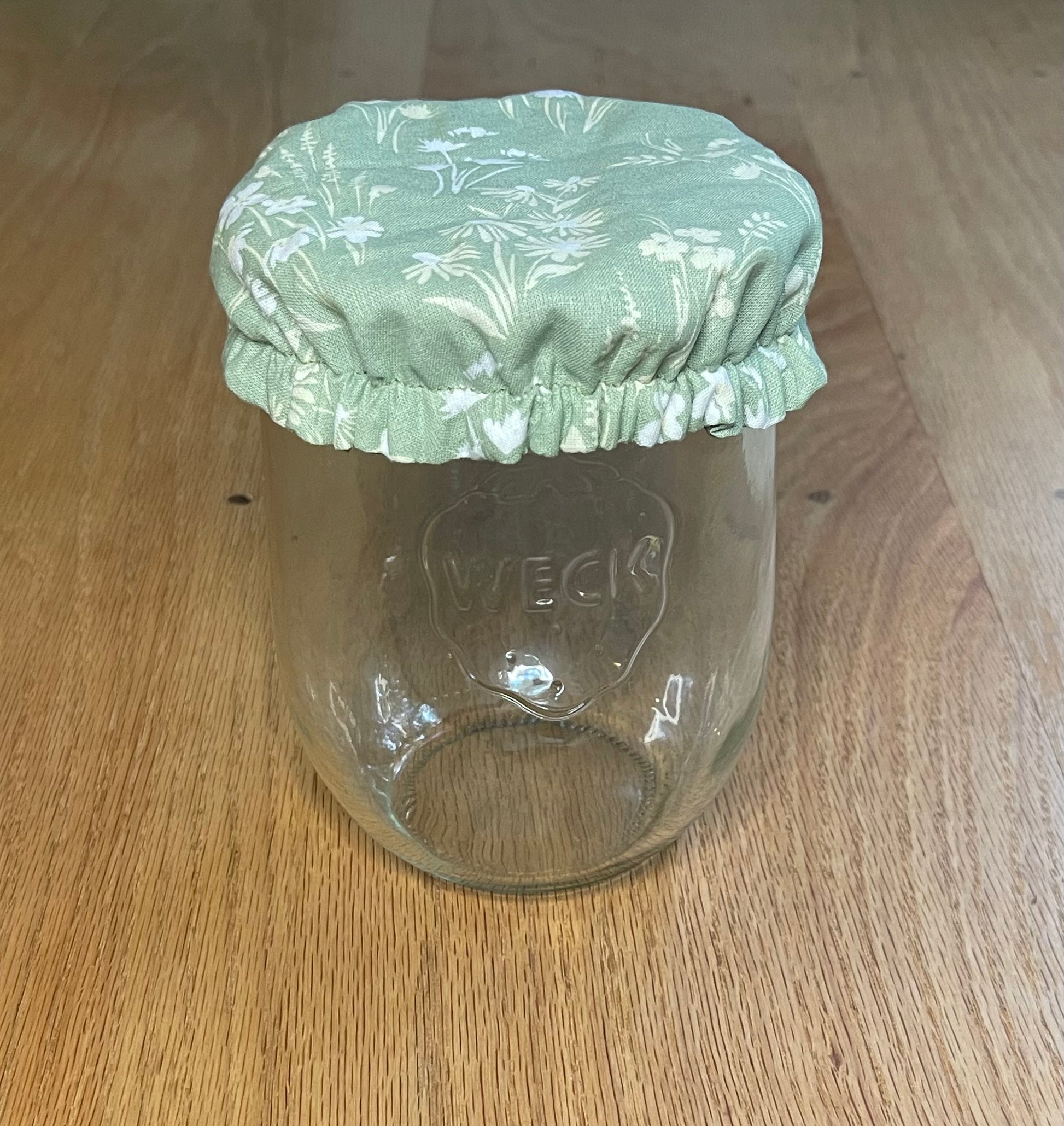 Clear glass jar with a green floral jar cover on a wooden surface Jar cover is meant for sourdough or sourdough starter.
