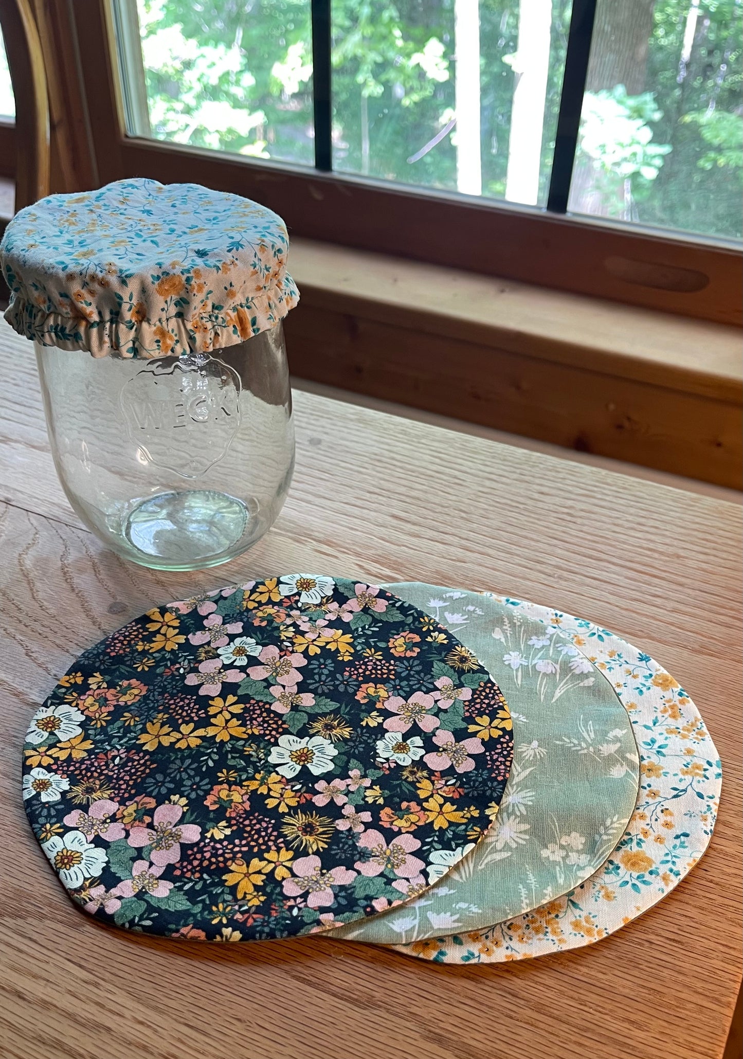 View of 3 different options for a handmade jar cover for sourdough. Set of floral jar covers with a glass jar on a wooden surface.

