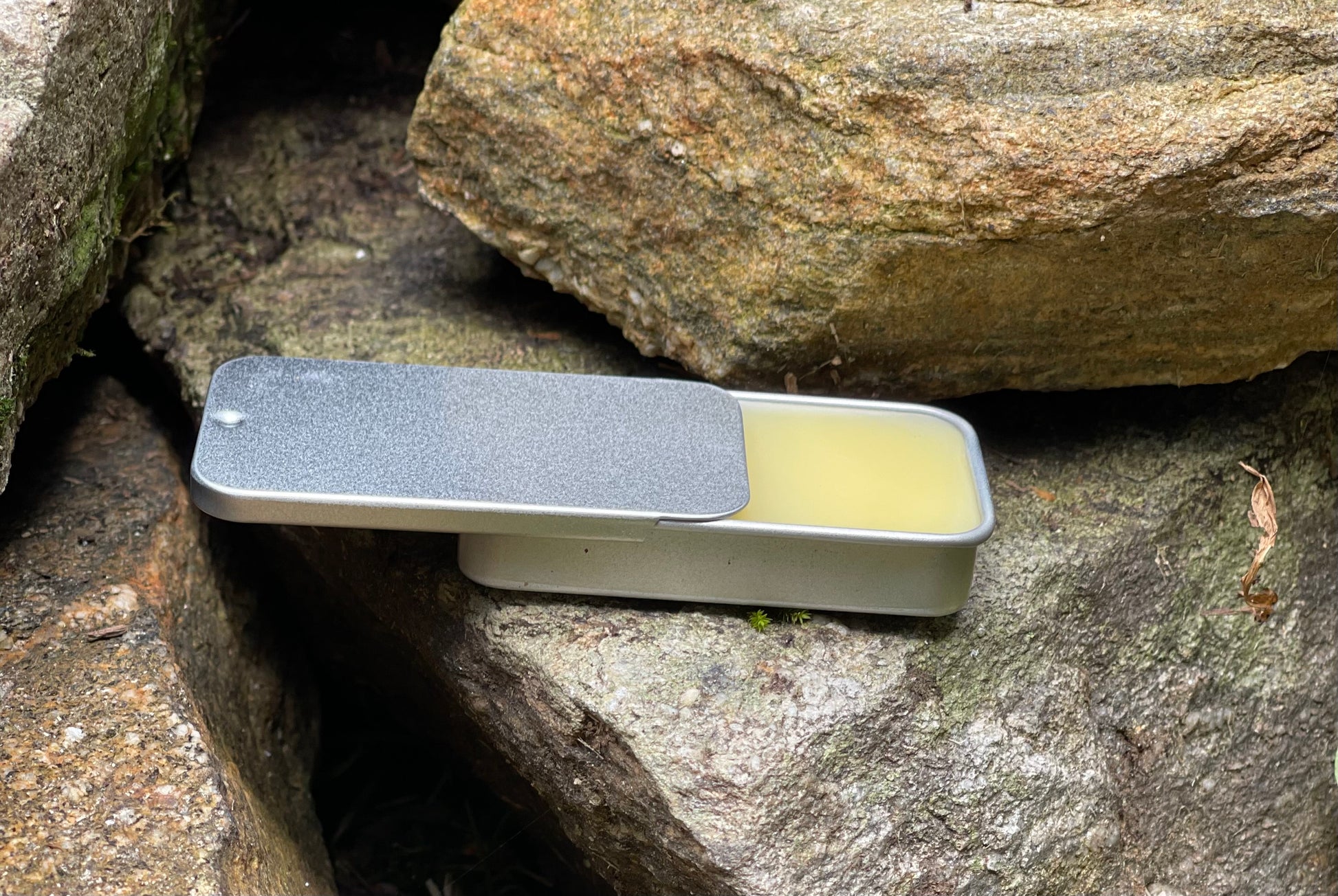 Side view of a sliding silver tin filled with organic lip balm, a natural skincare product infused with beeswax and soothing oils.